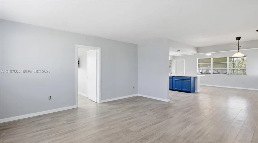 Open floor plan featuring wood-finish flooring, neutral wall paint, multi-pane windows, and a peninsula-style kitchen counter with blue cabinetry