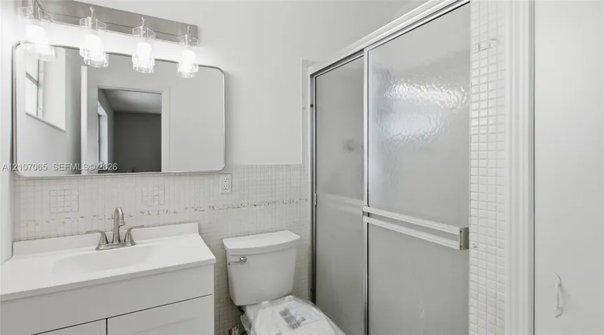 Bathroom featuring a white vanity cabinet, square wall-mounted mirror, four-light vanity fixture, and a shower enclosure with sliding glass doors