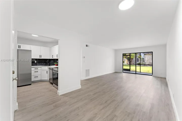 Kitchen featuring white shaker cabinetry, stainless steel appliances, and dark tile backsplash, complemented by wood-finish flooring and floor-to-ceiling glass sliding doors