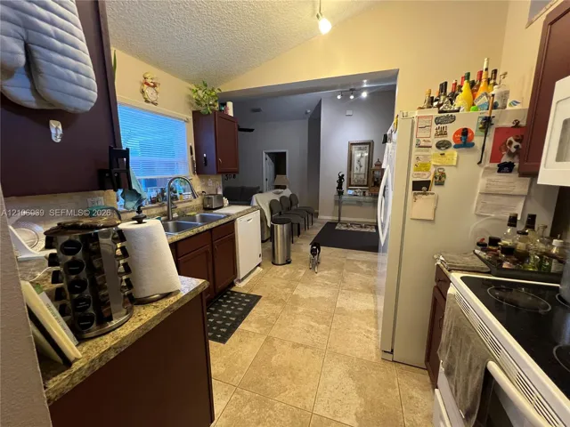 Kitchen featuring dark-toned cabinetry, stone-finish countertops, stainless steel dual-basin sink, tile flooring, and vaulted ceilings