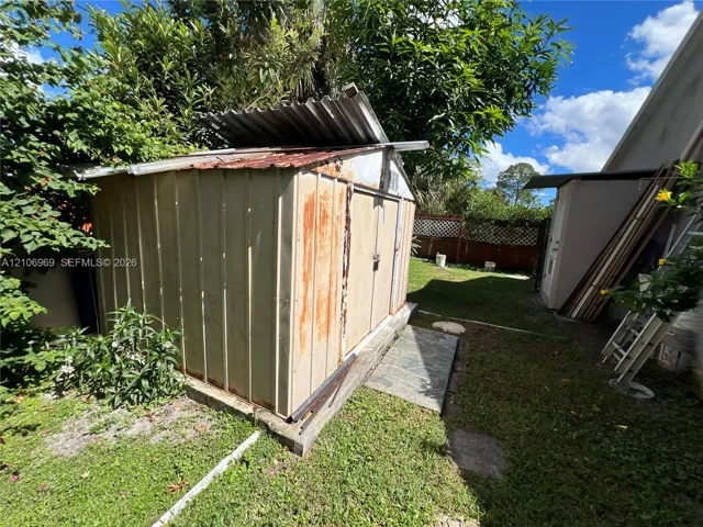 Exterior storage structure featuring a corrugated metal roof, vertical steel siding, and a concrete foundation pad situated within a grass-covered backyard