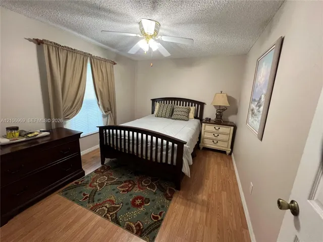 Room featuring wood-finish flooring, textured ceiling, and a central ceiling fan with integrated lighting