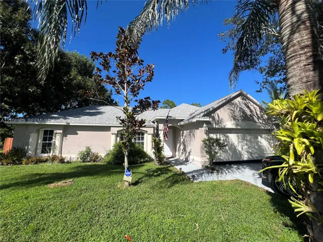 Single-story exterior featuring light-toned stucco siding, a multi-gabled roofline, decorative pillars, and an attached two-car garage