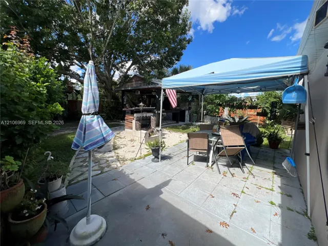 Rear patio featuring large-format concrete pavers, a stone-accented outdoor bar, and a covered timber-framed structure