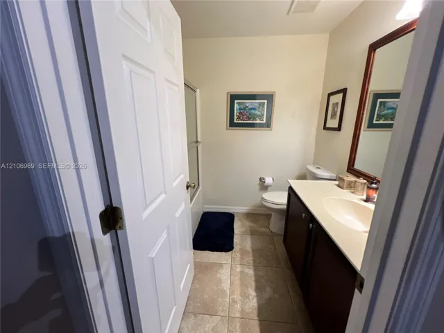 Bathroom featuring a vanity with a solid-surface countertop and integrated sink, dark wood-tone cabinetry, a framed wall mirror, and neutral-toned floor tile