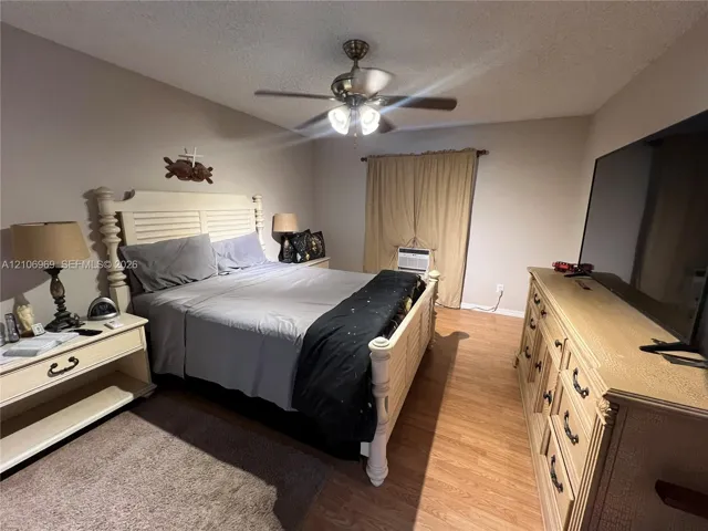 Neutral interior room featuring wood-finish flooring and a central ceiling fan with integrated lighting
