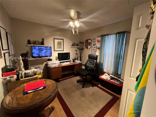 Room with wood-finish flooring, ceiling-mounted light fixture with fan, and window featuring curtain hardware