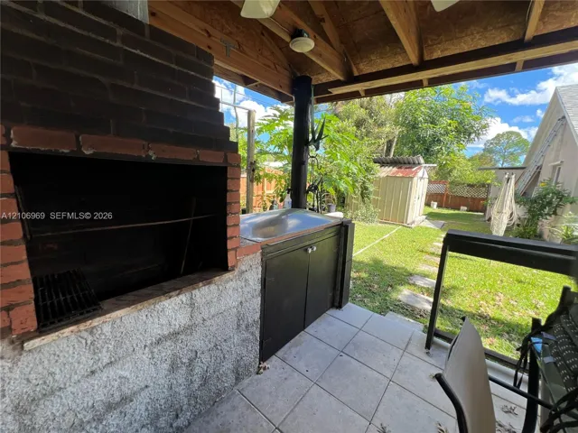 Covered outdoor kitchen featuring a built-in masonry grill, tiled flooring, exposed wood ceiling beams, and integrated cabinetry