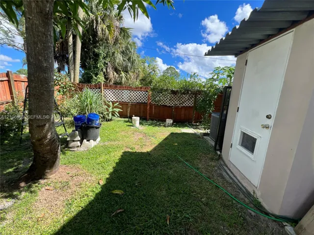 Backyard featuring a wood-panel fence with lattice detailing, grass lawn, and mature trees
