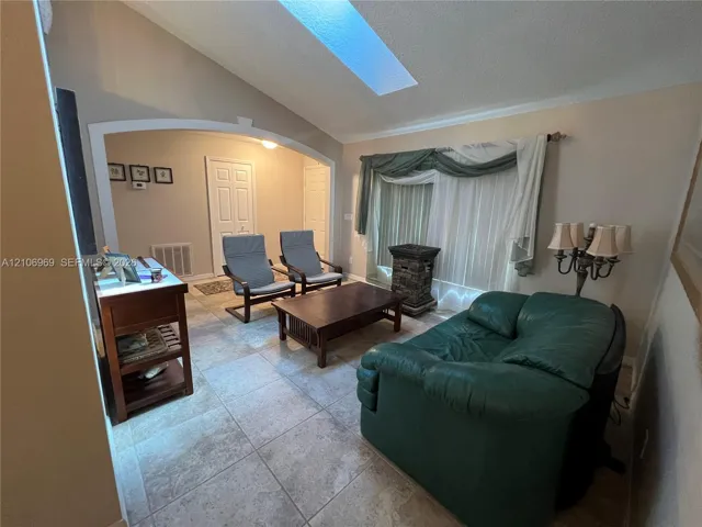 Vaulted ceiling featuring a large rectangular skylight, arched architectural opening, and tile flooring