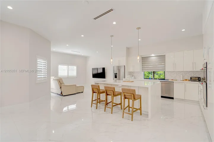 Kitchen featuring high-gloss cabinetry, stone-finish countertops, waterfall-edge island, polished tile flooring, and recessed lighting