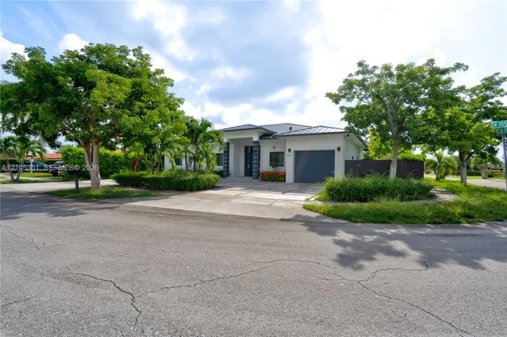 Single-story exterior featuring a metal roof, attached garage, stone-accented entryway, and mature landscaping