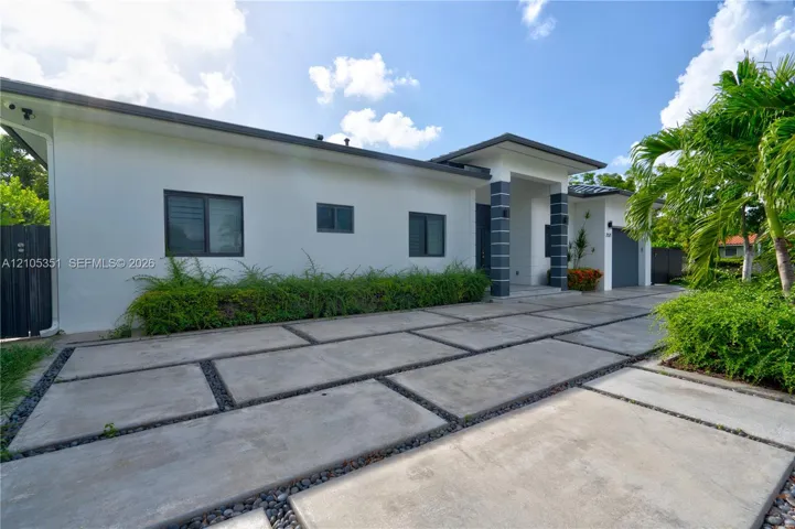 Contemporary exterior featuring smooth stucco finish, geometric concrete paver driveway with decorative stone accents, covered entryway with stone-clad columns, and single-car garage