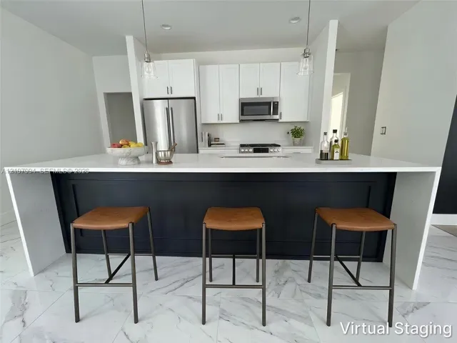 Kitchen featuring a waterfall-edge island with a dark-tone base, white shaker-style cabinetry, stainless steel appliances, and large-format tile flooring
