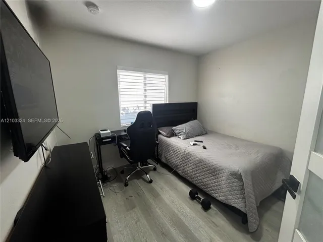 Bedroom featuring wood-finish flooring, a neutral color palette, and a window with horizontal blinds