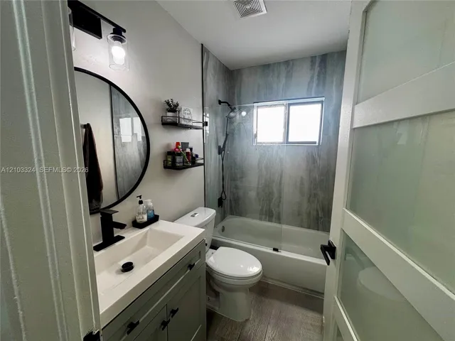 Bathroom featuring a vanity with a rectangular sink and matte black faucet, a round wall-mounted mirror, a tub-shower combination with floor-to-ceiling surround, and a glass-paneled sliding door