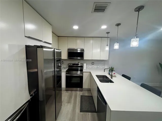 Kitchen featuring flat-panel cabinetry, quartz countertops, a double-basin stainless steel sink with a pull-down faucet, stainless steel appliances, and wood-finish flooring