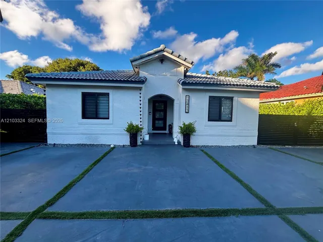 Stucco exterior with a tiled roof, arched entryway, and a concrete driveway featuring inlaid grass borders