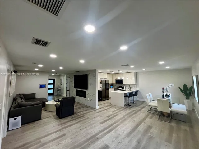 Open-concept interior featuring wood-finish flooring, recessed lighting, a stone-finish accent wall with an integrated fireplace, and a kitchen island with stone-finish countertops
