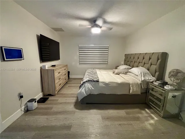 Neutral-toned interior featuring wood-finish flooring, a ceiling fan with integrated lighting, and horizontal window blinds