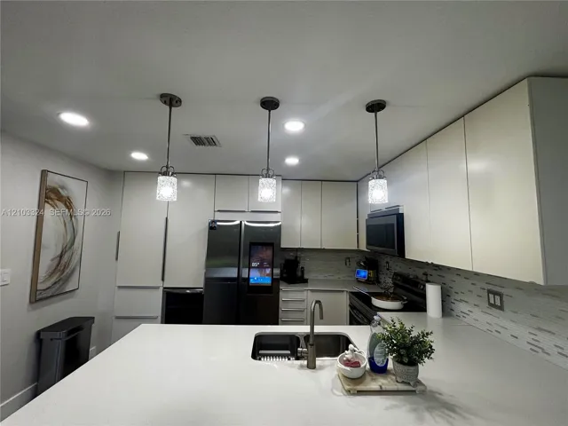 Kitchen featuring slab countertops, flat-panel cabinetry, recessed lighting, glass pendant fixtures, and a dual-basin undermount sink with a gooseneck faucet