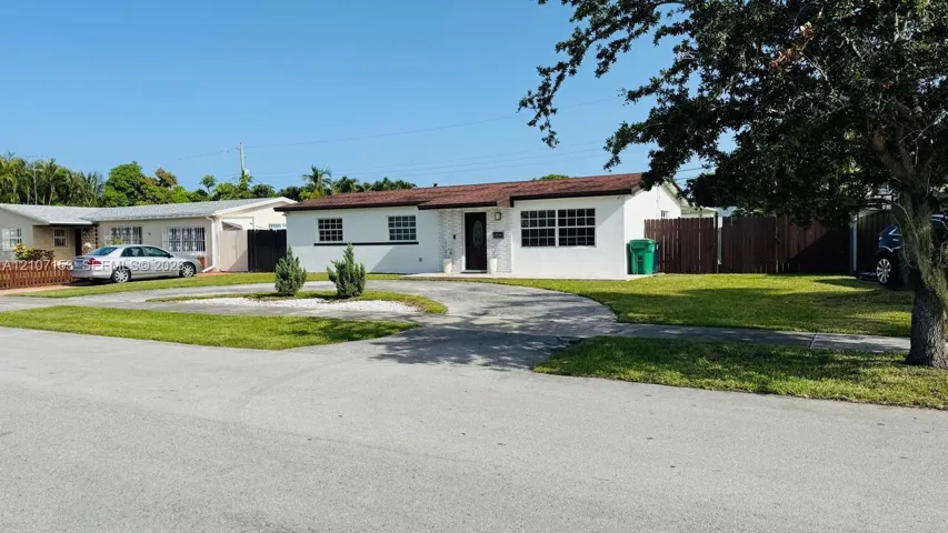 Single-story exterior featuring a white stucco facade, multi-paned windows, a circular concrete driveway, and wood-panel privacy fencing