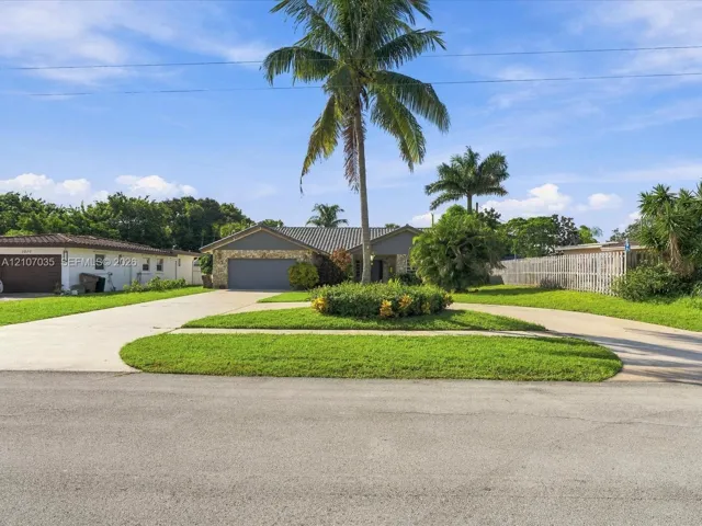 featuring a stone facade, multi-car garage, circular concrete driveway, and mature landscaping