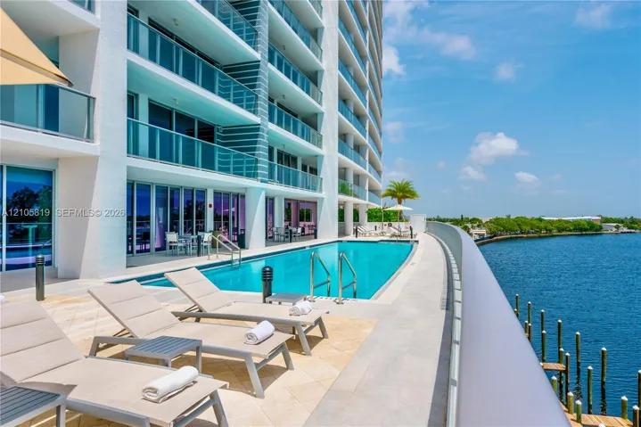 Heated Pool Overlooking Middle River. Waterfront terrace featuring a rectangular swimming pool, stone-tile decking, and glass-railing balconies