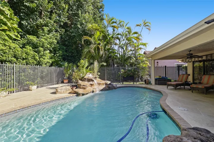Inground swimming pool with a stone water feature, covered patio, concrete deck, and metal perimeter fencing