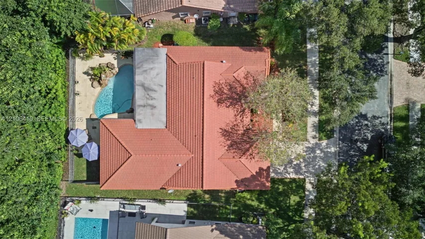 Aerial perspective featuring a tile roof, an in-ground pool with a stone water feature, paved walkways, and mature landscaping
