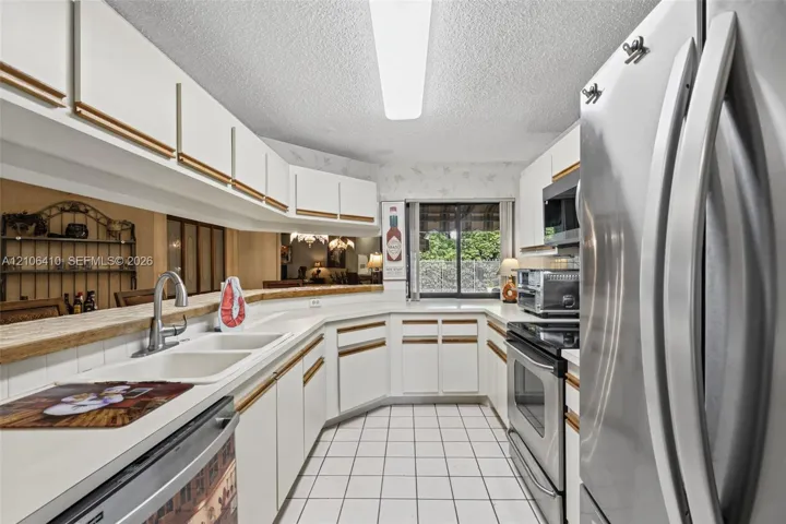 Kitchen featuring white cabinetry, stainless steel appliances, a dual-basin sink with a gooseneck faucet, tile flooring, and a breakfast bar