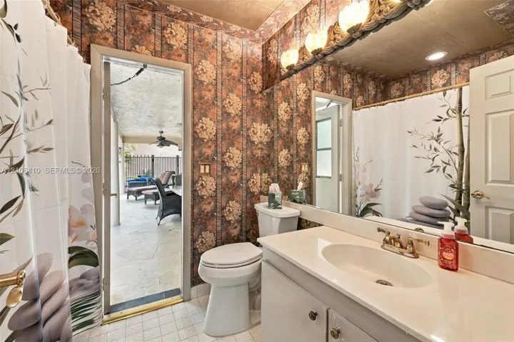 Bathroom featuring a solid-surface vanity countertop, drop-in sink with dual-handle faucet, full-width wall mirror, decorative light fixture, and tile flooring