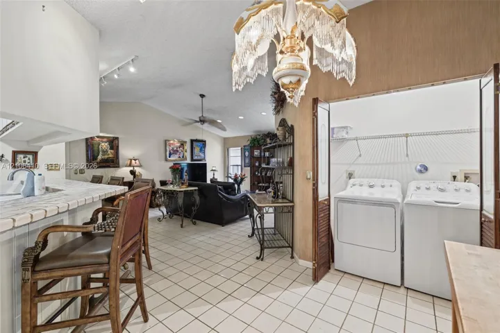 Vaulted ceiling with decorative chandelier, tile flooring, and integrated laundry closet with bifold doors