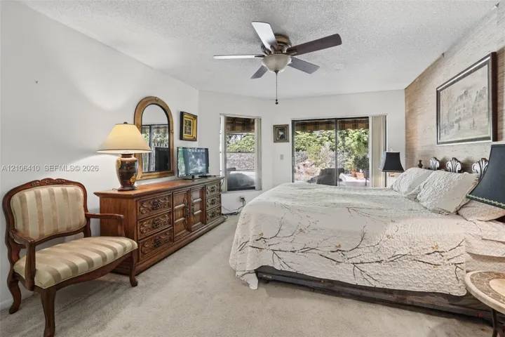 Bedroom featuring an accent wall with natural-finish horizontal wood paneling, sliding glass doors, a corner window, and a ceiling fan