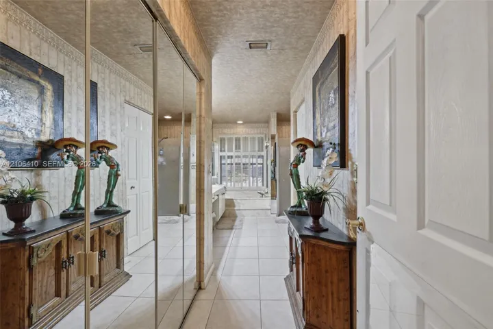 Hallway featuring full-height mirrored closet doors, tile flooring, crown molding, and a multi-pane window