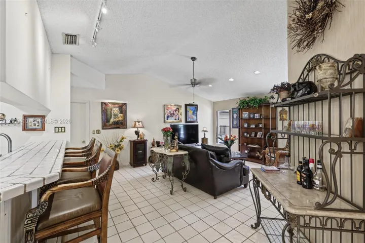 Living area featuring vaulted ceilings, tile flooring, and a built-in kitchen peninsula with a tiled countertop and breakfast bar seating