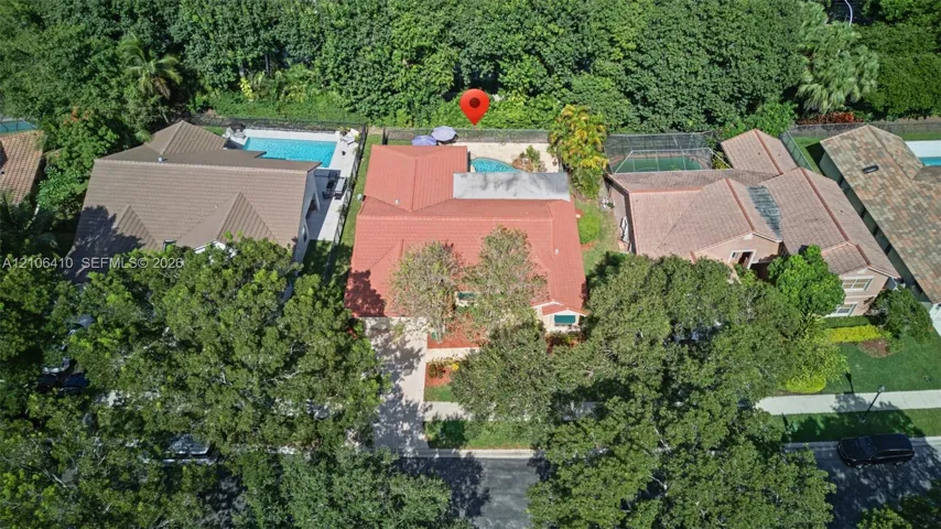 Aerial perspective featuring a tile roof, an in-ground swimming pool, mature tree canopy, and dense perimeter landscaping
