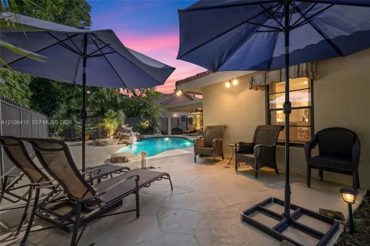 Flagstone patio featuring an in-ground pool with a natural stone water feature, exterior wall-mounted lighting, and a metal perimeter fence