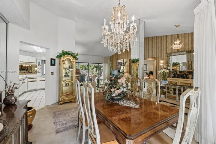 Dining area featuring vaulted ceilings, a central crystal chandelier, floor-to-ceiling mirror paneling, and textured wallpaper