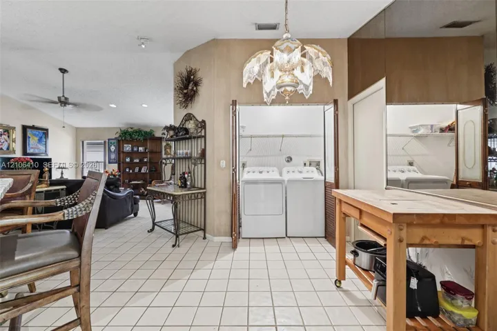 Ceramic tile flooring, vaulted ceilings, and built-in laundry closet with bi-fold doors, accented by decorative chandelier lighting and mirrored wall paneling