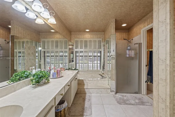Dual-sink vanity with integrated countertop, recessed lighting, glass-enclosed shower, built-in soaking tub with surround, and large-format tile flooring