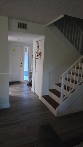 Entryway featuring wood-finish flooring, a white paneled front door with a side light window, and a staircase with white balusters and dark-toned treads
