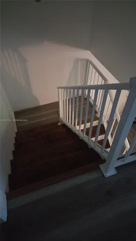 Staircase featuring dark-stained wooden treads, white railing with vertical balusters, and grey wood-finish flooring