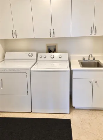 Laundry area featuring white cabinetry, a built-in utility sink with a stone-finish countertop, and tiled flooring