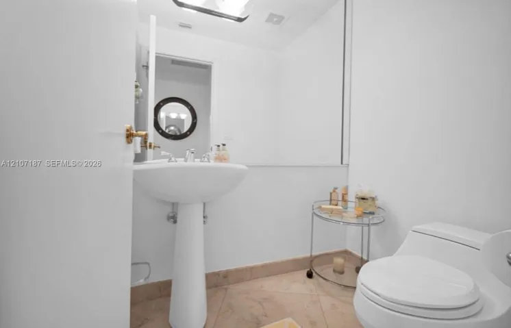 Pedestal sink with polished metal faucet, large wall-mounted mirror, and tile flooring