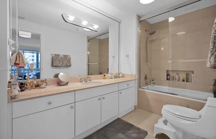 Full-width vanity with stone countertop, large-scale wall-mounted mirror, soaking tub with glass enclosure, tiled shower surround, and integrated wall niche