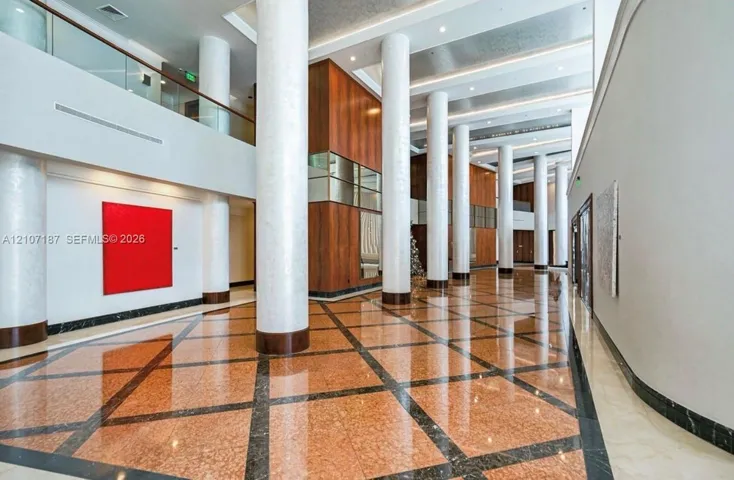 Grand atrium featuring soaring ceilings, polished stone tile flooring with geometric inlay, full-height decorative columns, and extensive wood-paneled wall accents