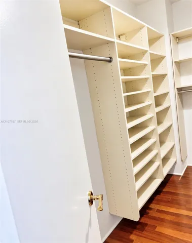 Custom walk-in closet featuring extensive built-in shelving, vertical storage partitions, integrated hanging rods, and wood-finish flooring