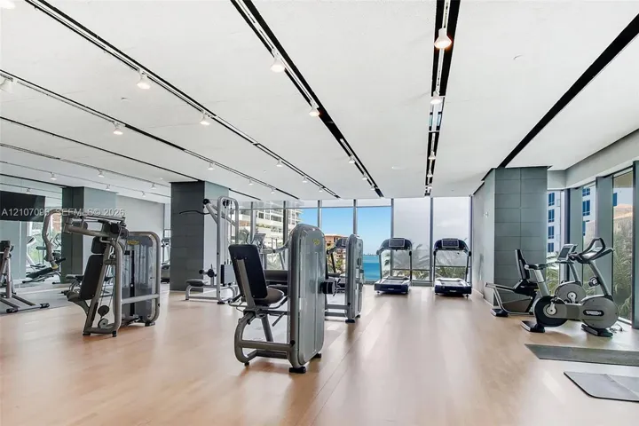 Fitness center featuring floor-to-ceiling windows, wood-finish flooring, recessed track lighting, and tiled structural columns