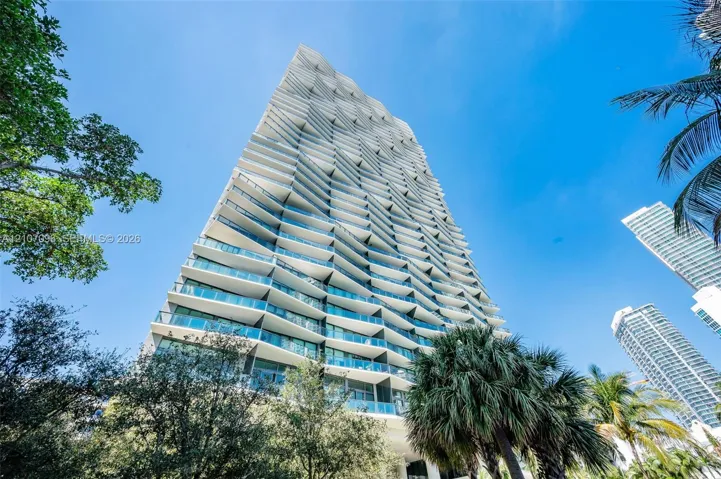 High-rise building featuring a geometric facade, undulating balconies with glass railings, and floor-to-ceiling glass windows